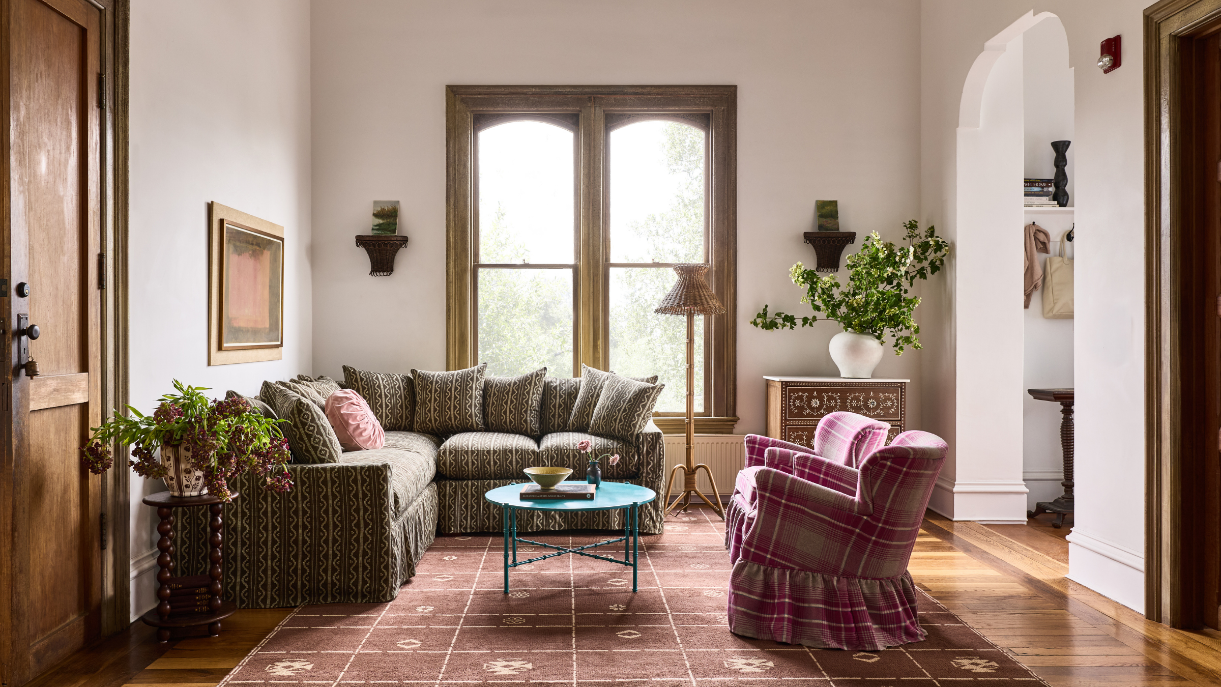 Sofagarnitur mit botanischem Muster, abgebildet in einem charaktervollen Wohnzimmer mit einem Teppich mit geometrischem Muster, einem Akzentstuhl mit Gingham-Röcken und großen Fenstern mit Holzrahmen