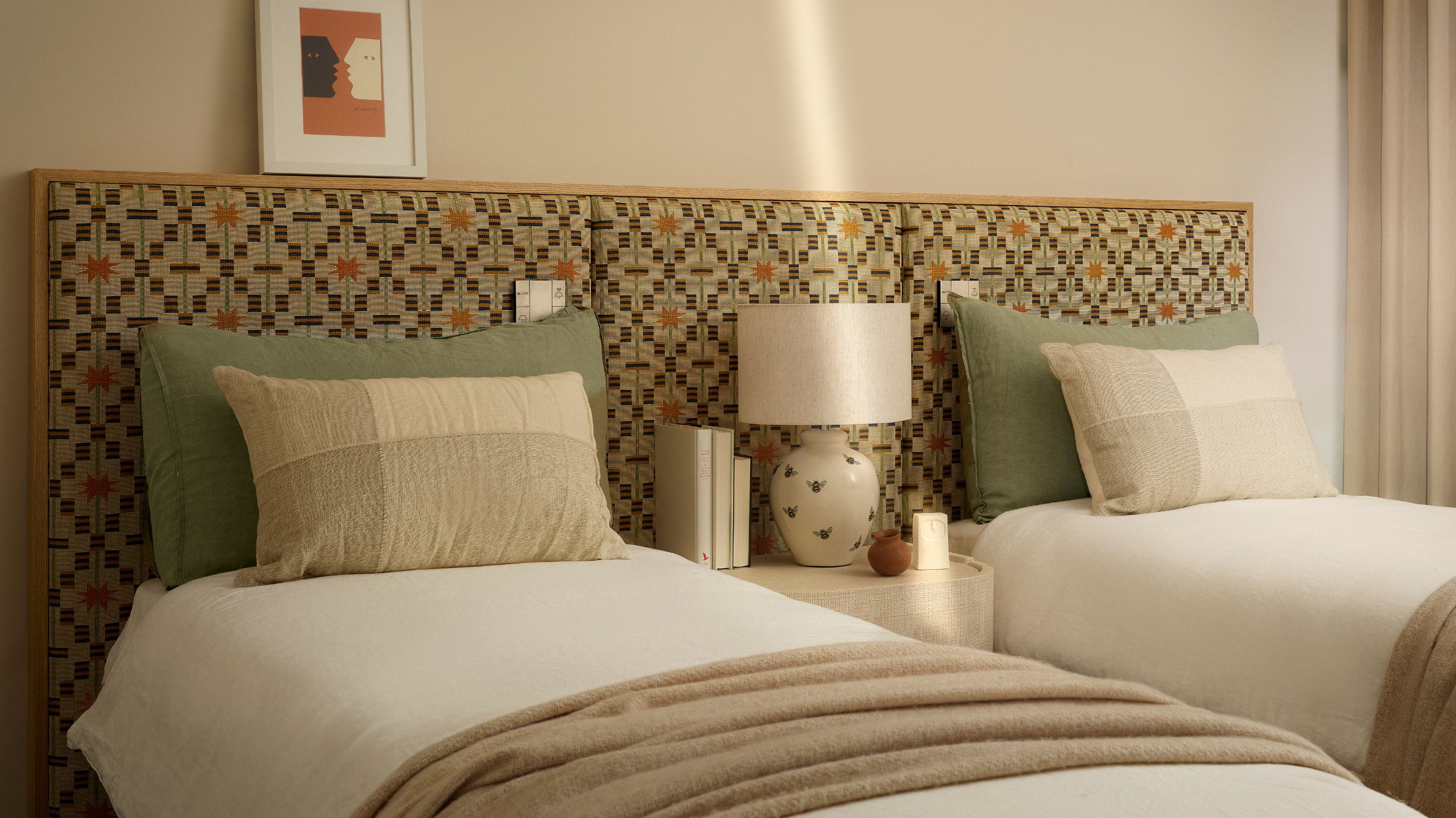 Zweibettzimmer mit gemustertem Kopfteil, salbeifarbenen Kissen und weißer Bettwäsche mit neutralen Wänden.