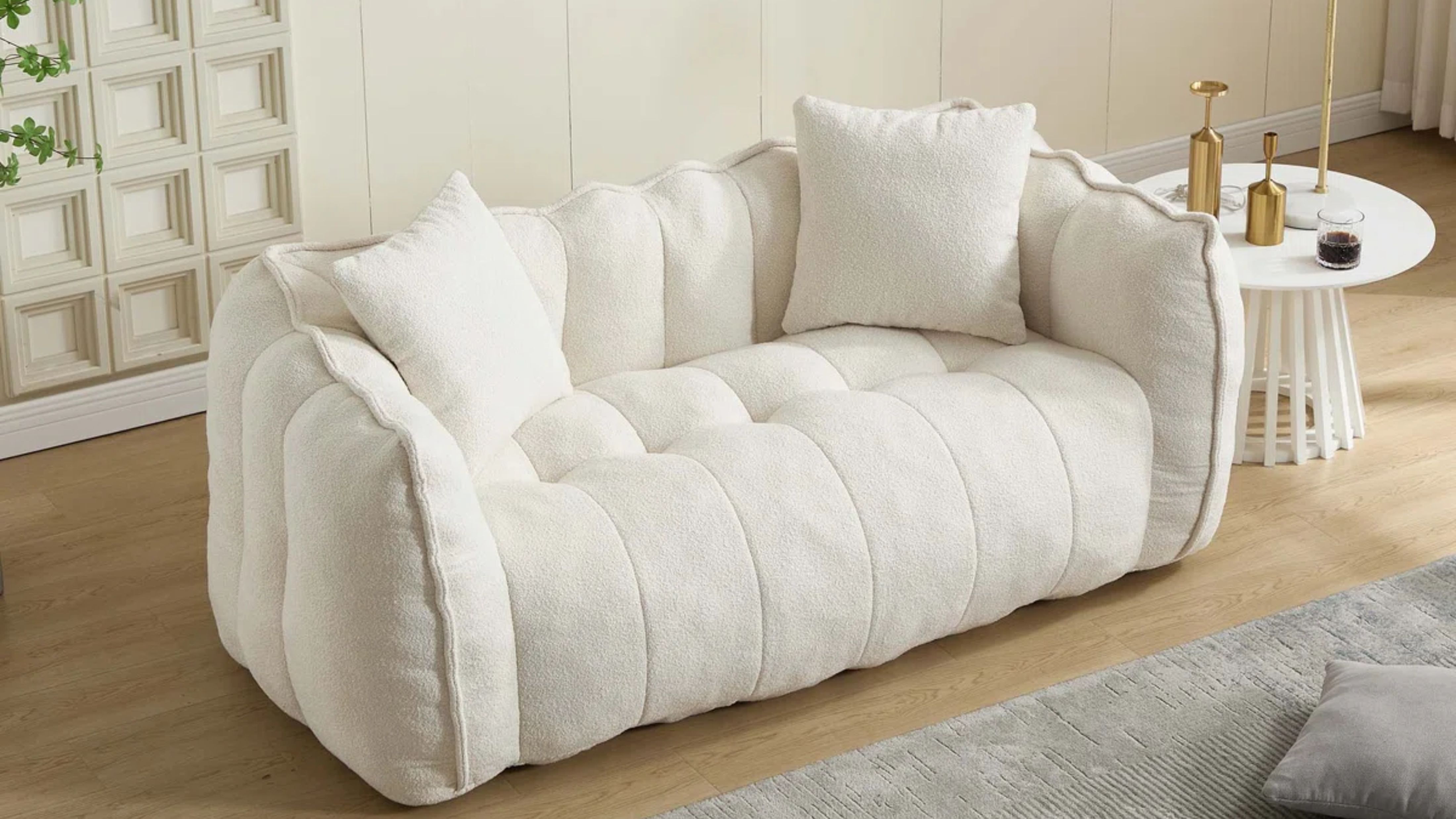Kleiner cremefarbener Kanal mit getuftetem 'ohne Knochen' Sofa im Wohnzimmer mit Holzboden, grauem Teppich und skulpturalem Beistelltisch mit verschiedenen Messinggegenständen