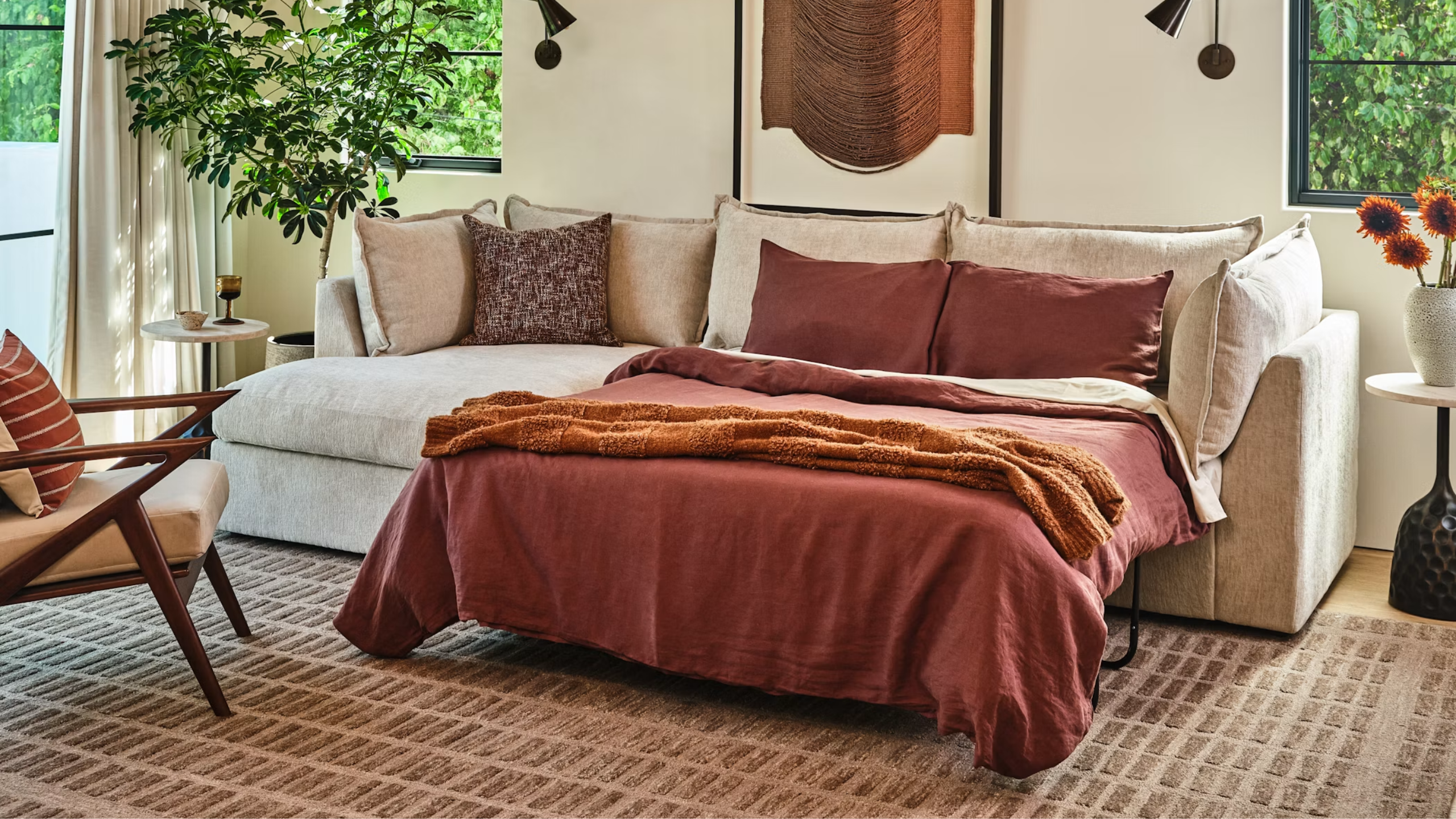 Gemütliches, neutrales Wohnzimmer mit einem geometrisch gemusterten Teppich und einem hellbeigen Schlafsofa mit Ochsenblut-Bettwäsche