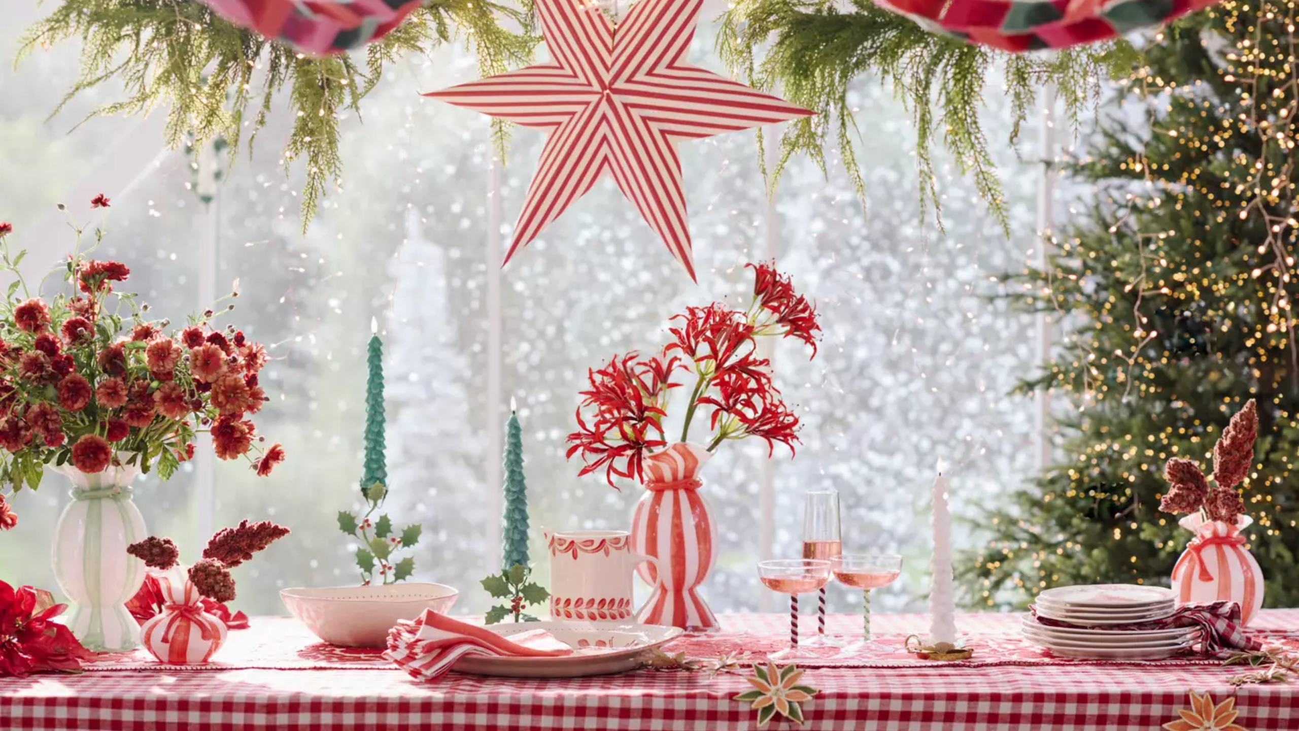 Festive tablescape featuring a red plaid tablecloth, candy-cane striped ceramic tableware and pendant lights, twisted evergreen taper candles, and warm string lights softly aglow in the background.