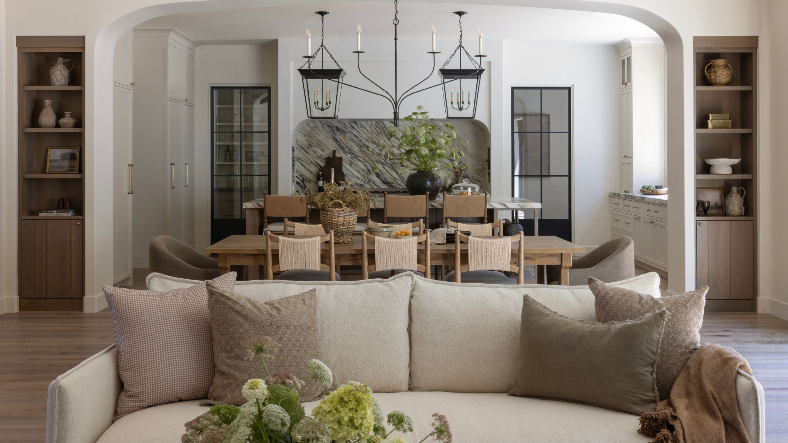 Blick vom Wohnzimmer auf einen offenen Ess- und Küchenbereich mit einer neutralen Couch vorne und in der Mitte, einer mehrschichtigen Küche mit Marmorrückwand und einer großen Insel