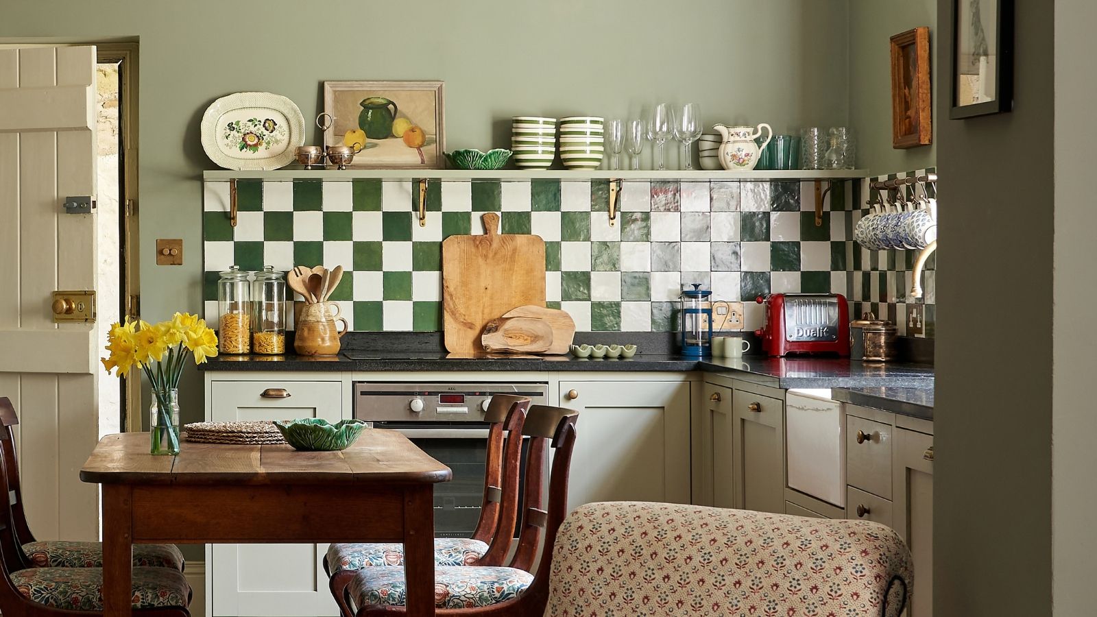 An open plan kitchen with dark walls and cabinets painted Pigeon by Farrow &amp; Ball and a green and white checkerboard backsplash