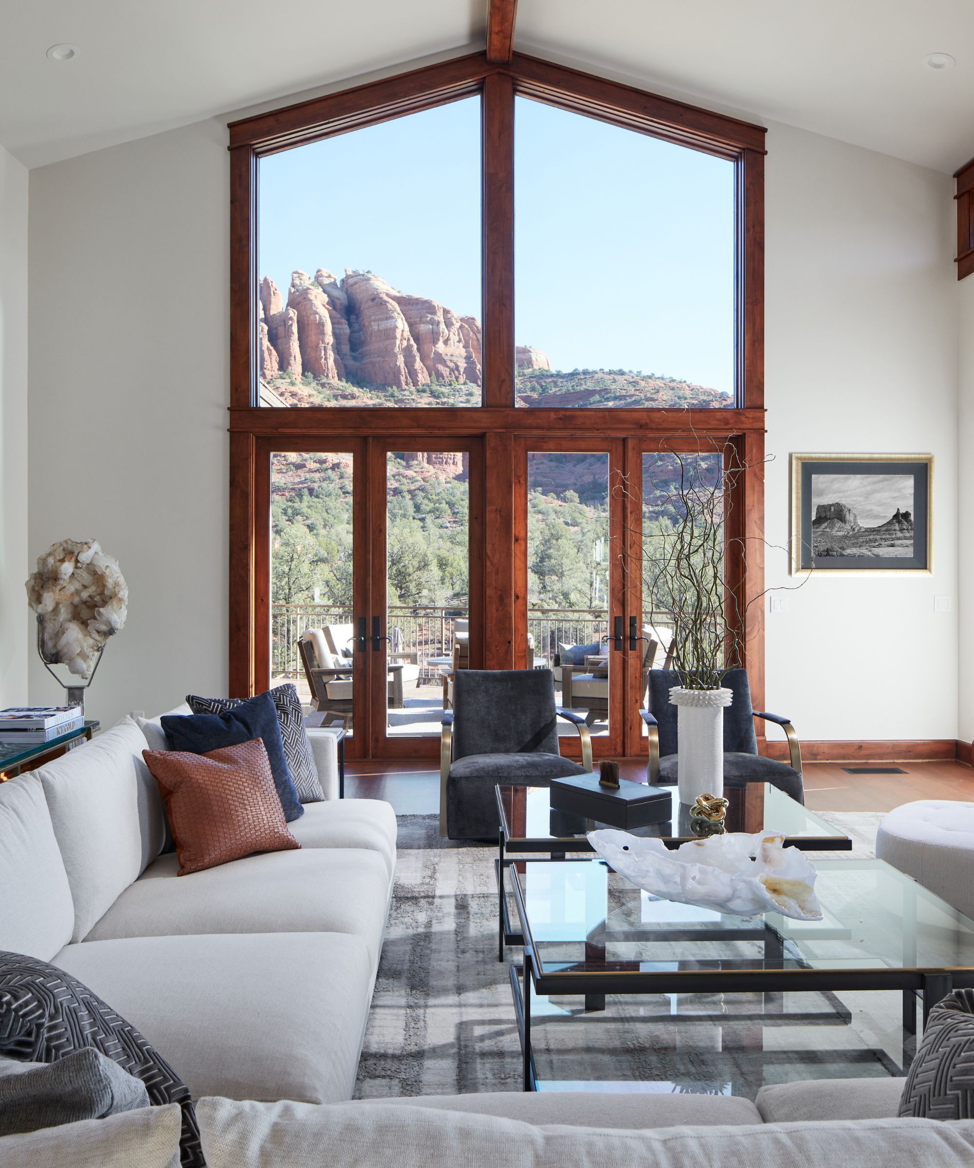Großes Wohnzimmer mit raumhohen Fenstern mit Holzrahmen und Blick auf die Berge. Cremefarbenes Sofa, graue Sessel, Couchtisch aus Glas im Vordergrund