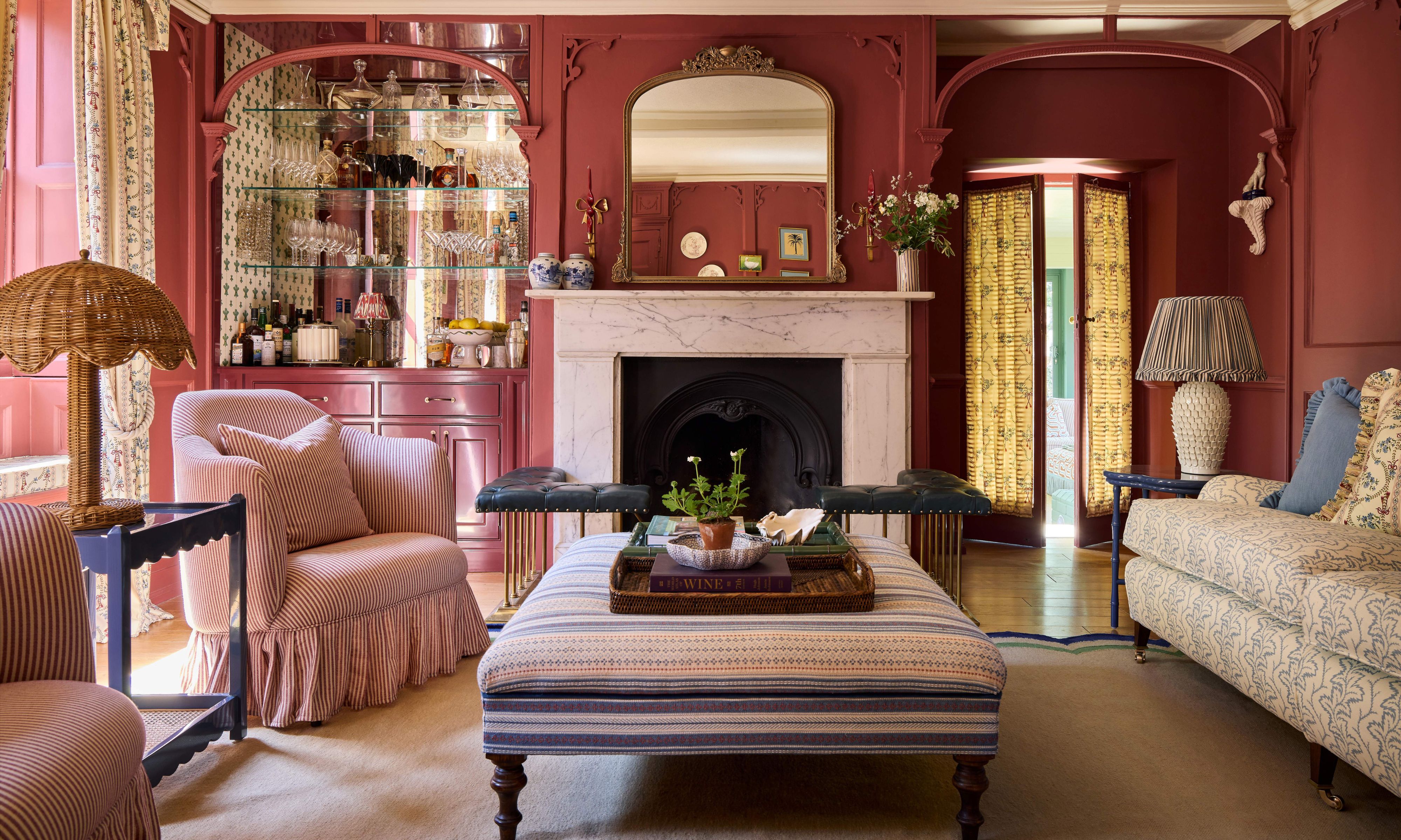 ein rot-rosa gestrichener historischer Salon mit Marmorkamin, maßgeschneiderter Hausbar, getäfelten Wänden und mehrschichtigen Möbeln und Mustern