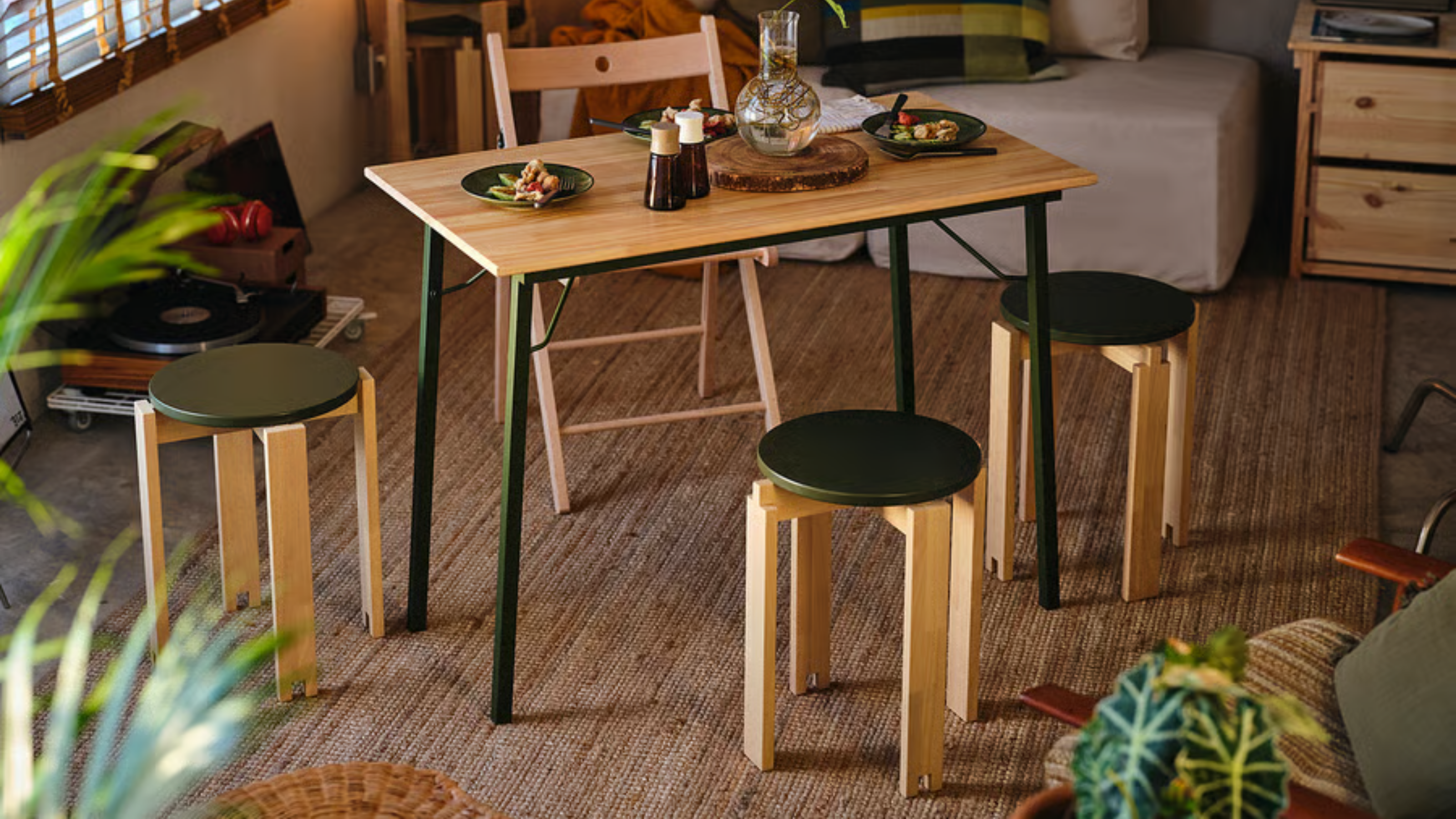 ein Wohnzimmer mit einem kleinen Tisch, drei Hockern, einem Klappstuhl und einem Juteteppich