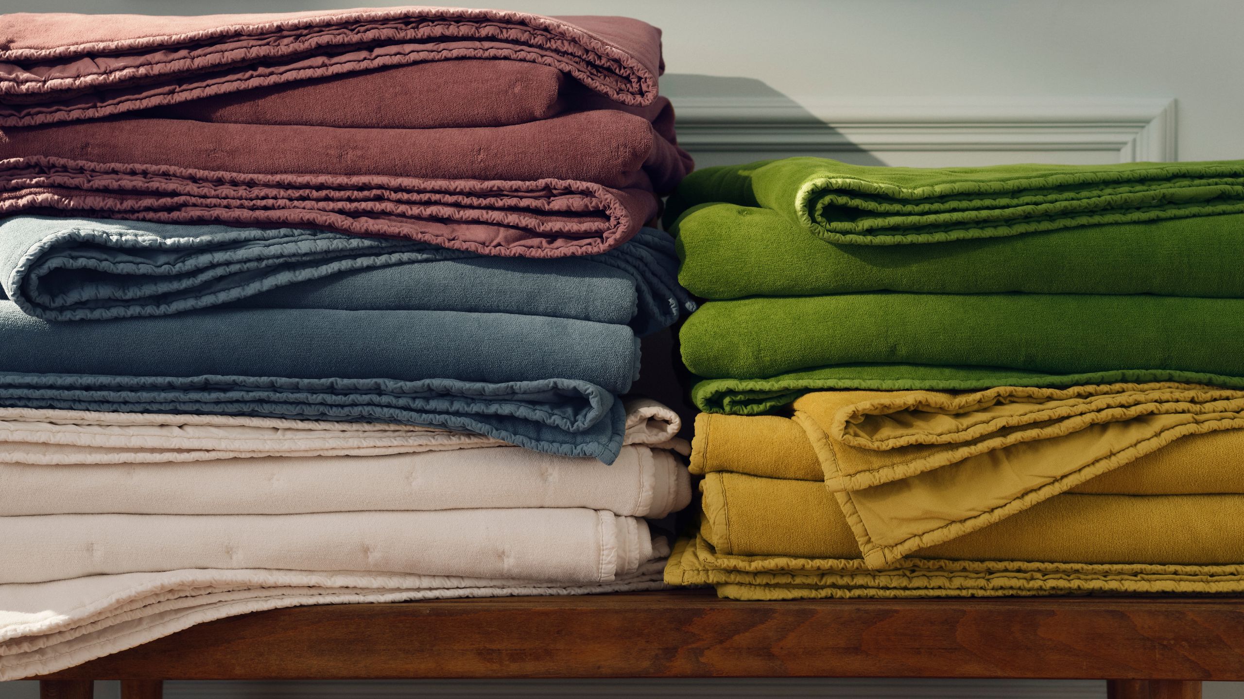 Fünf gewaschene Brooklinen-Samtdecken in allen Farben, zusammengefaltet auf einer Holzbank.