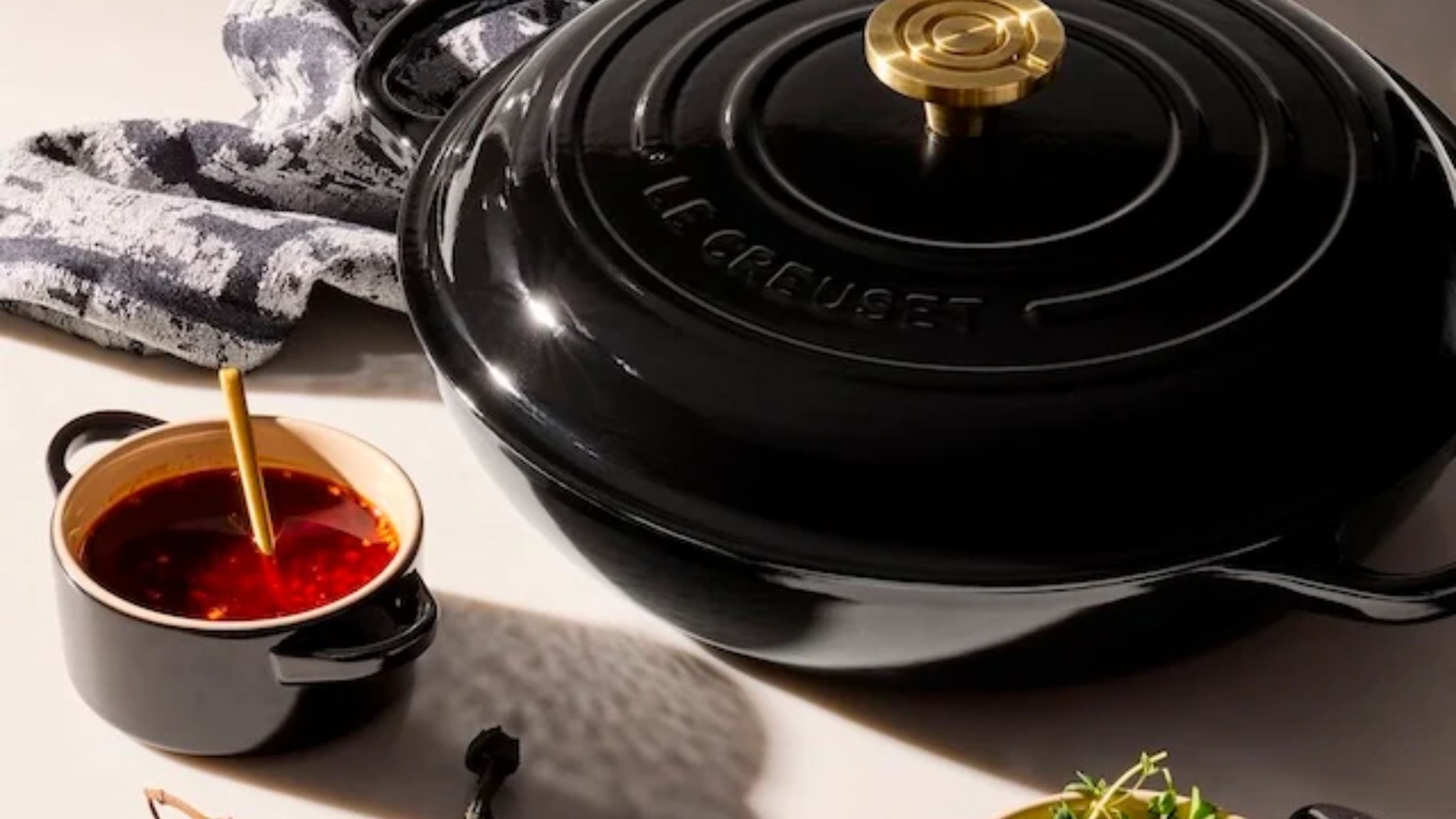 Ein polierter, tiefschwarzer Schmortopf von Le Creuset auf einem Tisch neben einer Mini-Cocotte
