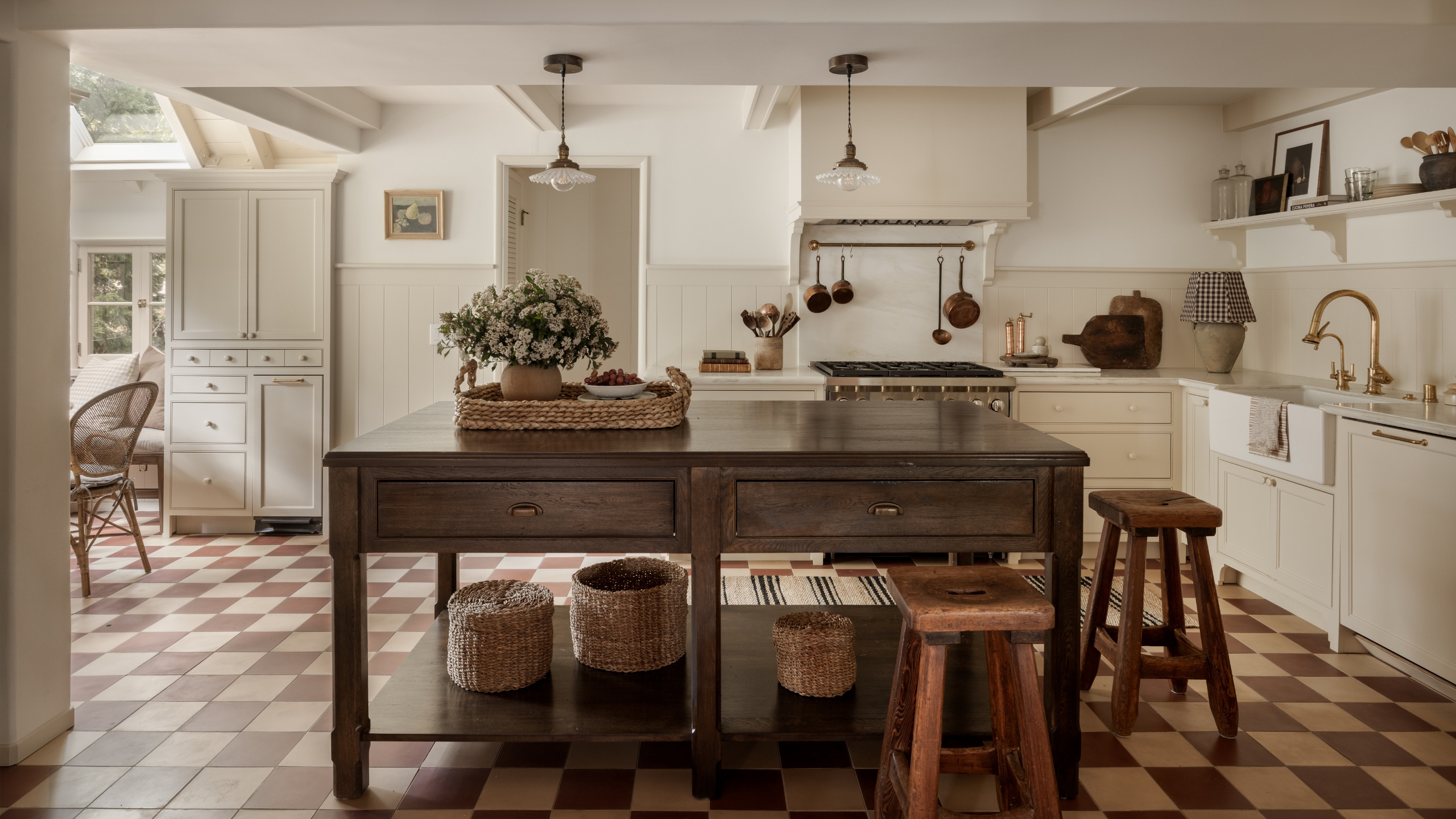 Eine weiße Küche mit einer freistehenden Kücheninsel aus dunklem Holz und einem beige-braunen Schachbrettboden