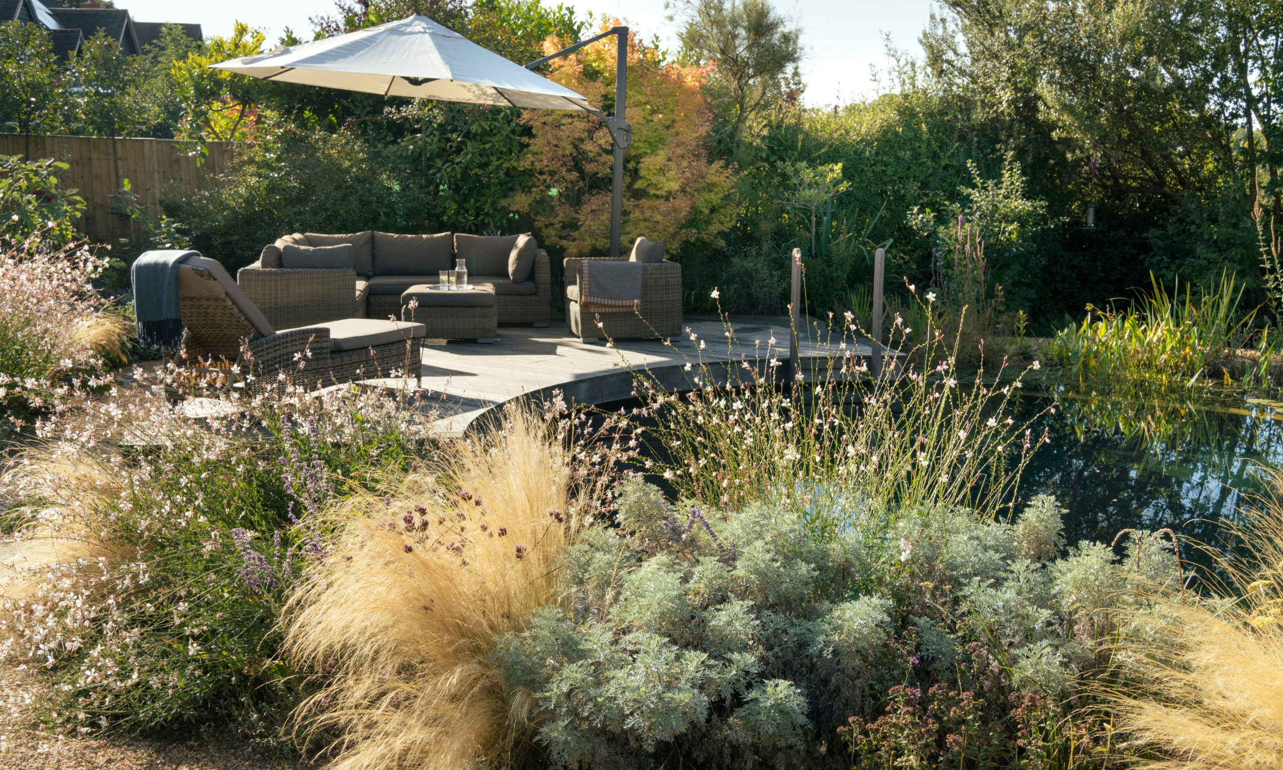 A natural garden swimming pond with chairs and sun loungers to the side on a wooden deck